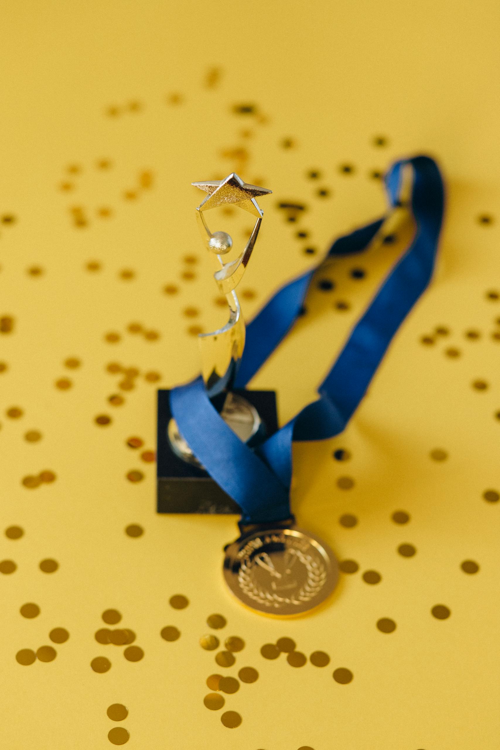 A golden trophy and medal with blue ribbon on a confetti-strewn yellow surface, symbolizing victory and achievement.