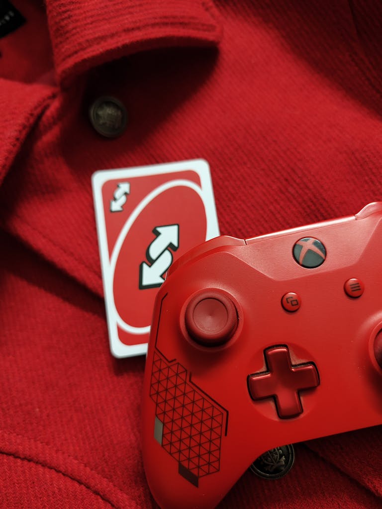 A red Xbox controller with a reverse Uno card on a red fabric background, perfect for gaming themes.