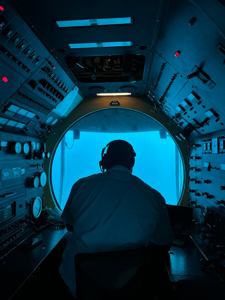 Operator in submarine control room analyzing equipment and blue ocean view.